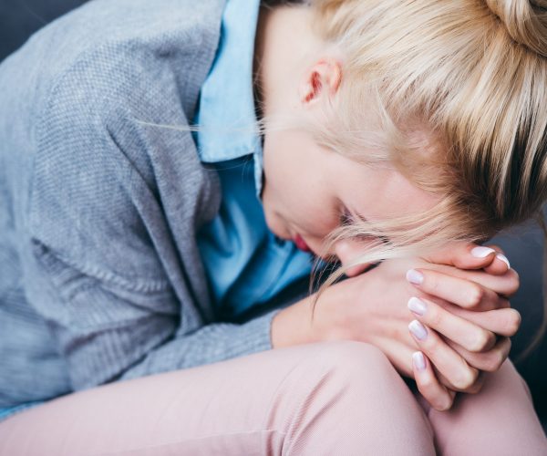 close up of sad woman with folded hands sitting at home