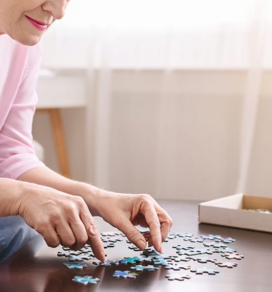 Alzheimer's disease and dementia prevention. Senior woman playing jigsaw puzzle on wooden table at home, mental health, empty space