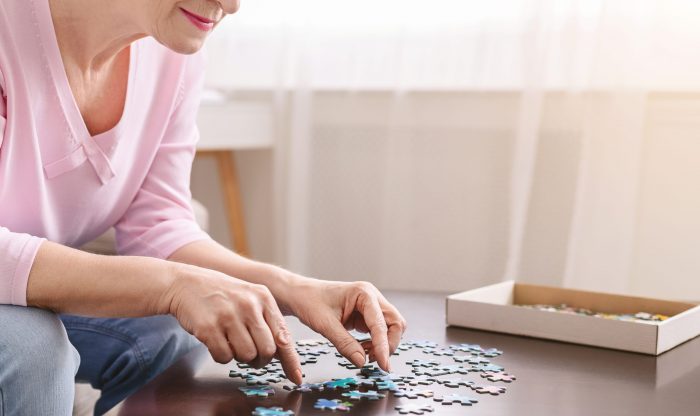 Alzheimer's disease and dementia prevention. Senior woman playing jigsaw puzzle on wooden table at home, mental health, empty space